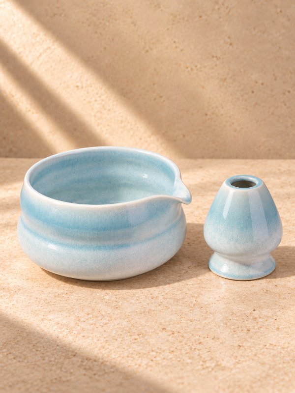 Błękitna ceramiczna czarka Kai z dzióbkiem i podstawka pod chasen, na beżowym kamieniu w smugach słońca